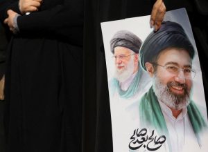 Mulher segura imagem do novo líder supremo do Irã, Mojtaba Khamenei, e do líder anterior, o ai...